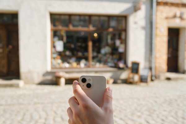 Dłoń ze smartfonem na tle witryny małego sklepu przy brukowanym rynku