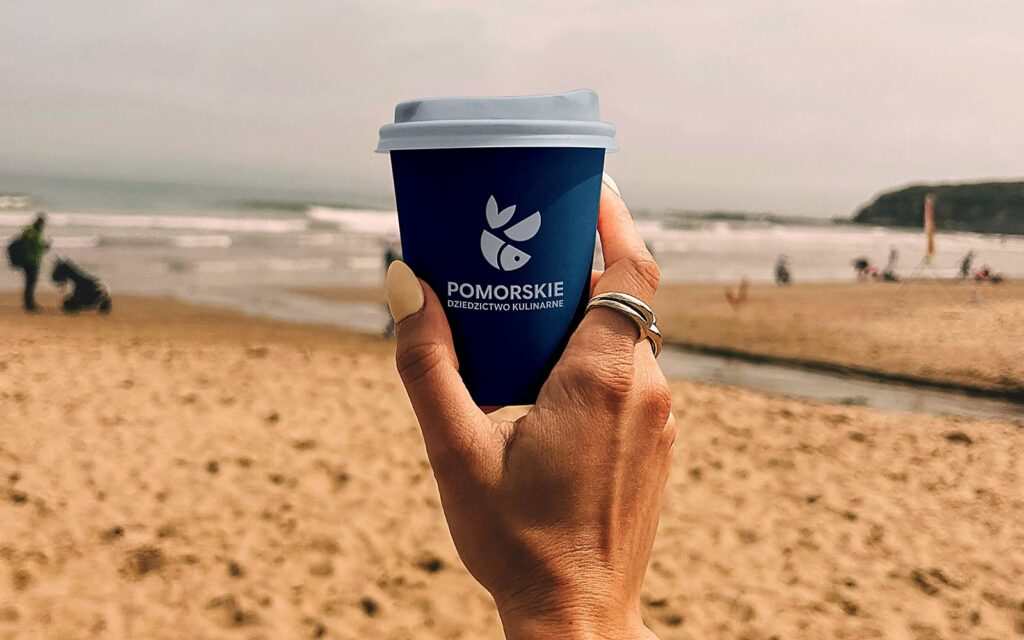 Kubek z logo Pomorskie Dziedzictwo Kulinarne na plaży - znak i identyfikacja wizualna
