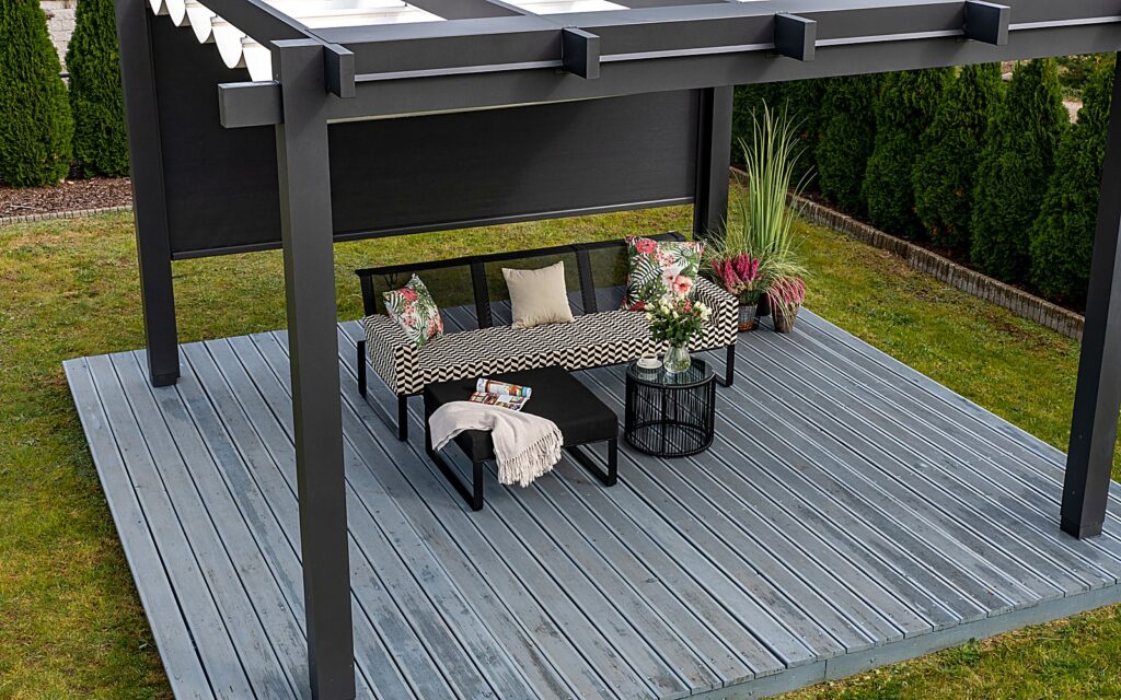 Nowoczesna pergola tarasowa z markizą nad drewnianym tarasem z leżanką - Terra Polska