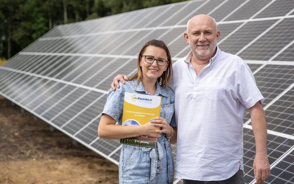 Dwie osoby z folderem oferty EkoKaszuby przed farmą fotowoltaiczną