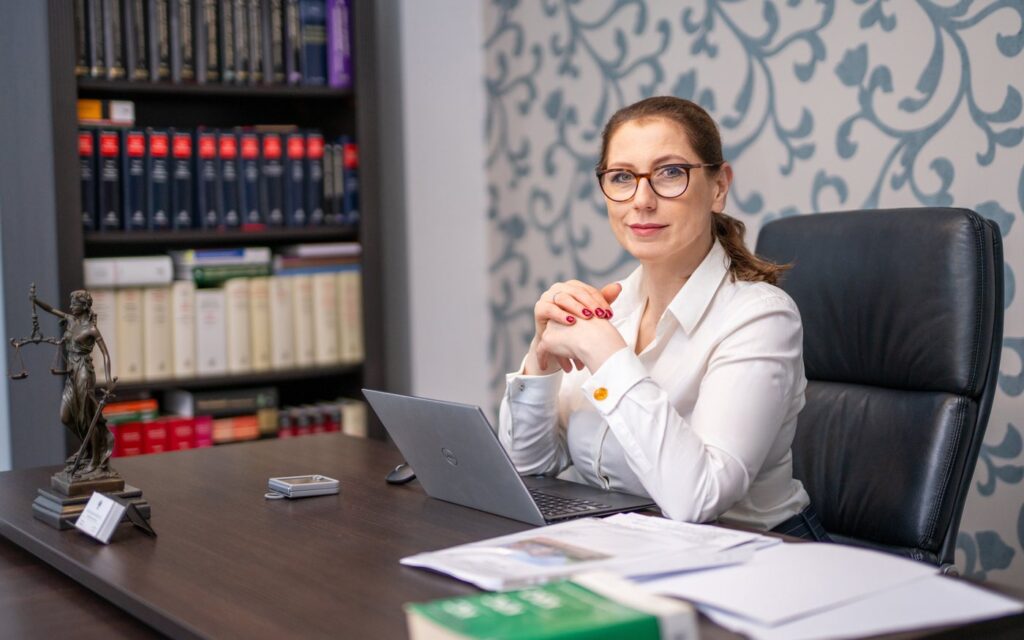Kobieta przy biurku w kancelarii notarialnej w Bytowie, obok figura Temidy i laptop