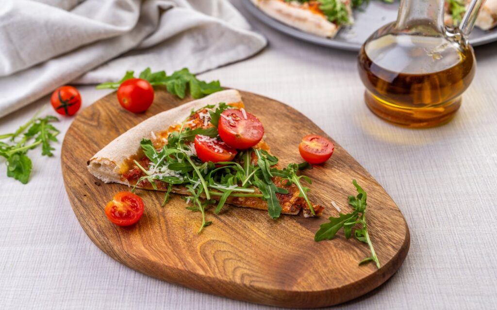 Kawałek pizzy z rukolą i pomidorkami koktajlowymi na drewnianej desce