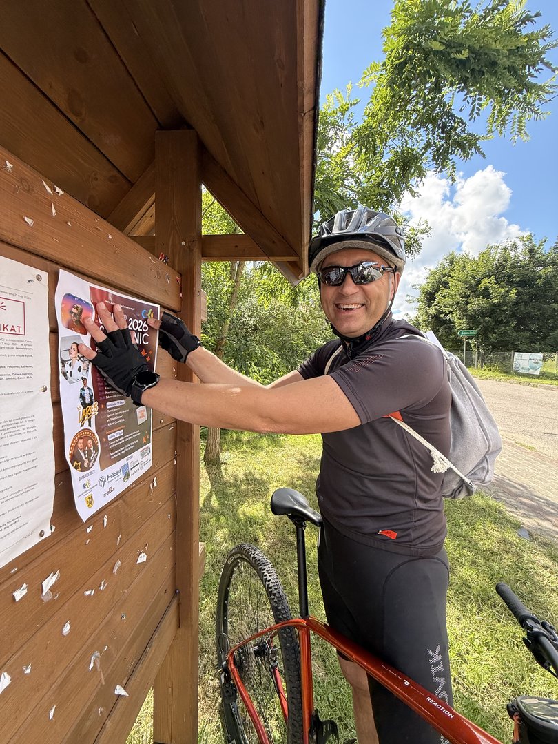 Wójt wiesza plakat na tablicy ogłoszeń, kadr z planu